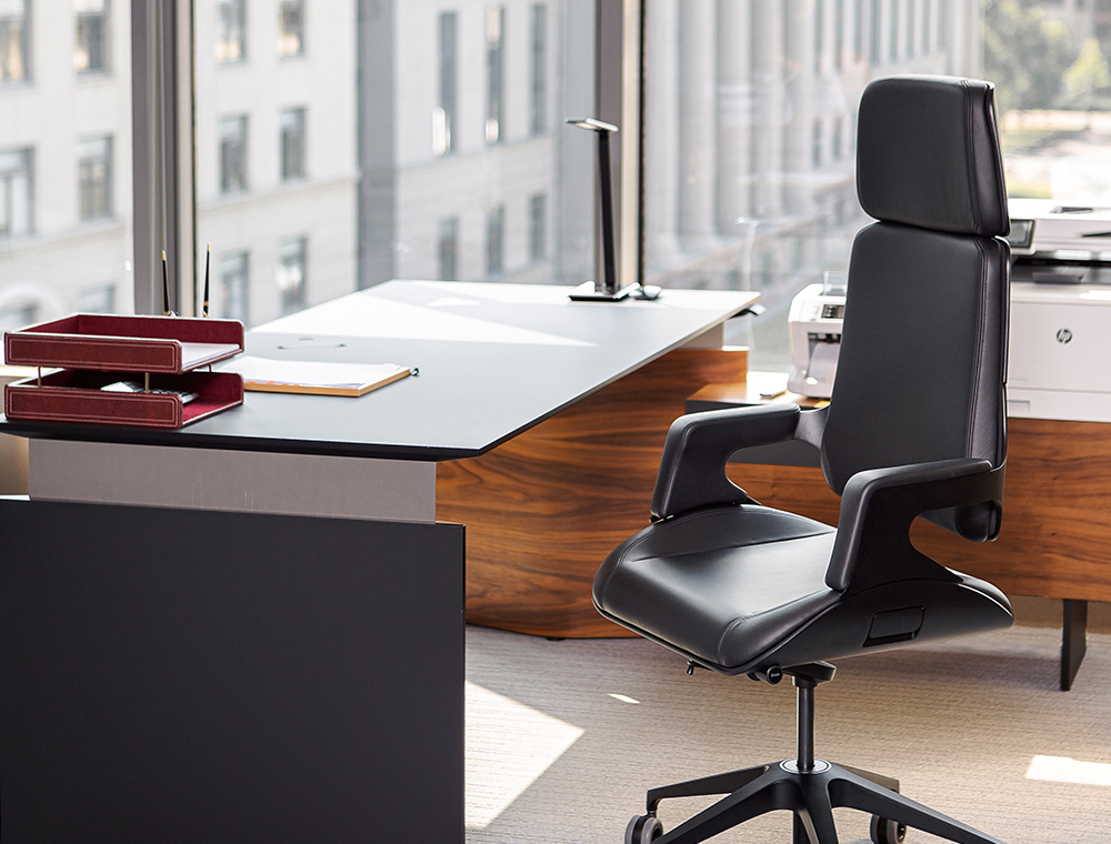 Un lujoso sillón giratorio SILVER con revestimiento de cuero blanco detrás de una mesa de escritorio con dos sillas giratorias enfrente en un despacho de dirección.