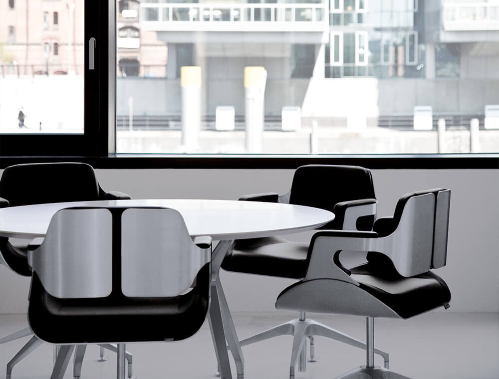 Nærbillede af et rundt bord med fire lave SILVER-designkontorstole med sort læderbetræk. 