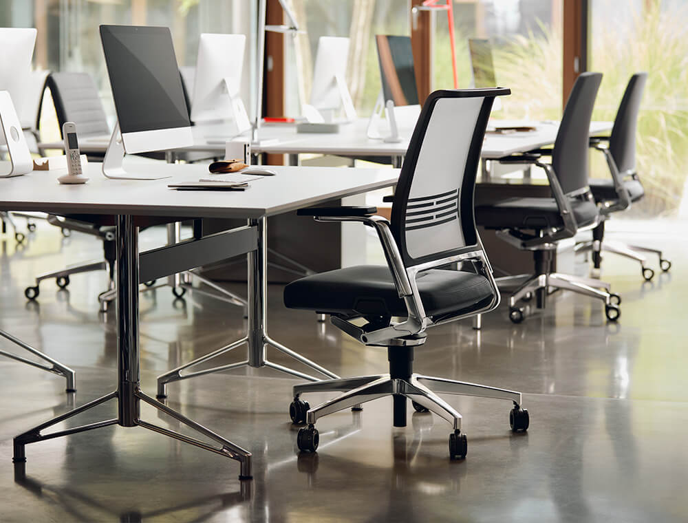Una oficina abierta con una silla giratoria VINTAGE con respaldo de malla en primer plano en el lugar de trabajo.