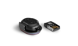 Small, round S 4.0 Active Sitting Solution sensor for office chairs in its black holder and the ANT receiver for the USB port on a computer. It prompts the user to change position and provides instructions for office workouts so that the user sits more healthily and ergonomically.