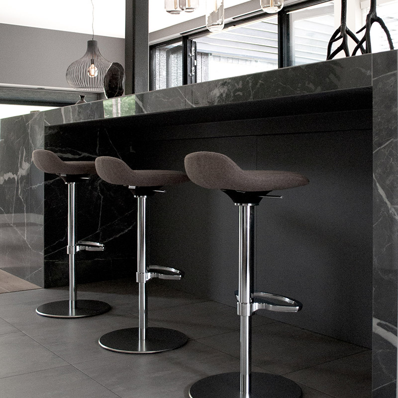 Three high-quality LIME bar stools with dark brown seat and backrest covers as well as chrome base frame, including functional footrest and sturdy base plate, in front of a black marble table in a modern lounge area | by studiokurbos  