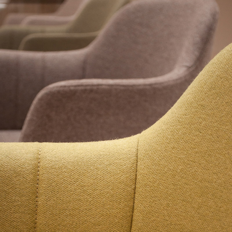 Close-up of the LEMON club chair with detailed illustration of the backrest cover with its elegant and forming seam contours. In the blurred background, we can see more chairs in different colours | by Interstuhl