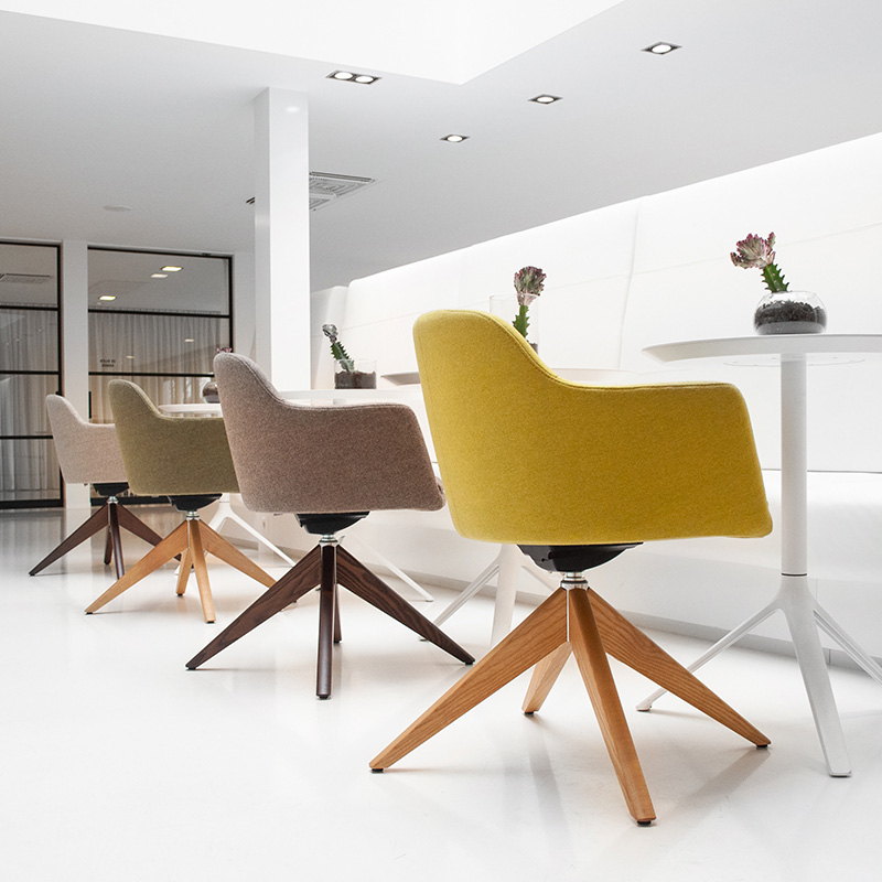 Stylish LEMON club chairs in a wide variety of coordinated colours and with different wooden base frames. They are positioned opposite a white bench with small tables and fill a modern lounge area | by Interstuhl