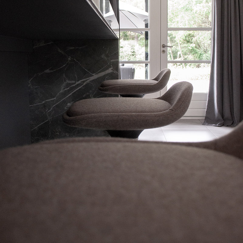Nærbillede af sæderne på tre barstole af typen LIME i brun foran et elegant, sort marmorbord i et værelse med dagslys | by studiokurbos
